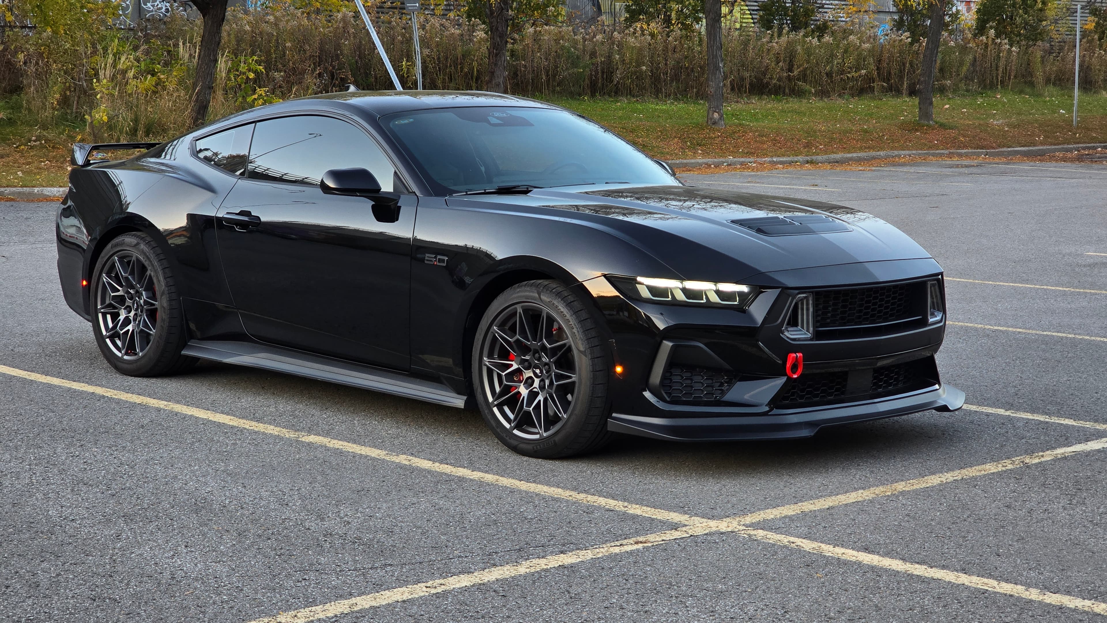 Black Ford Mustang with custom wheels and red tow hook parked in a lot.