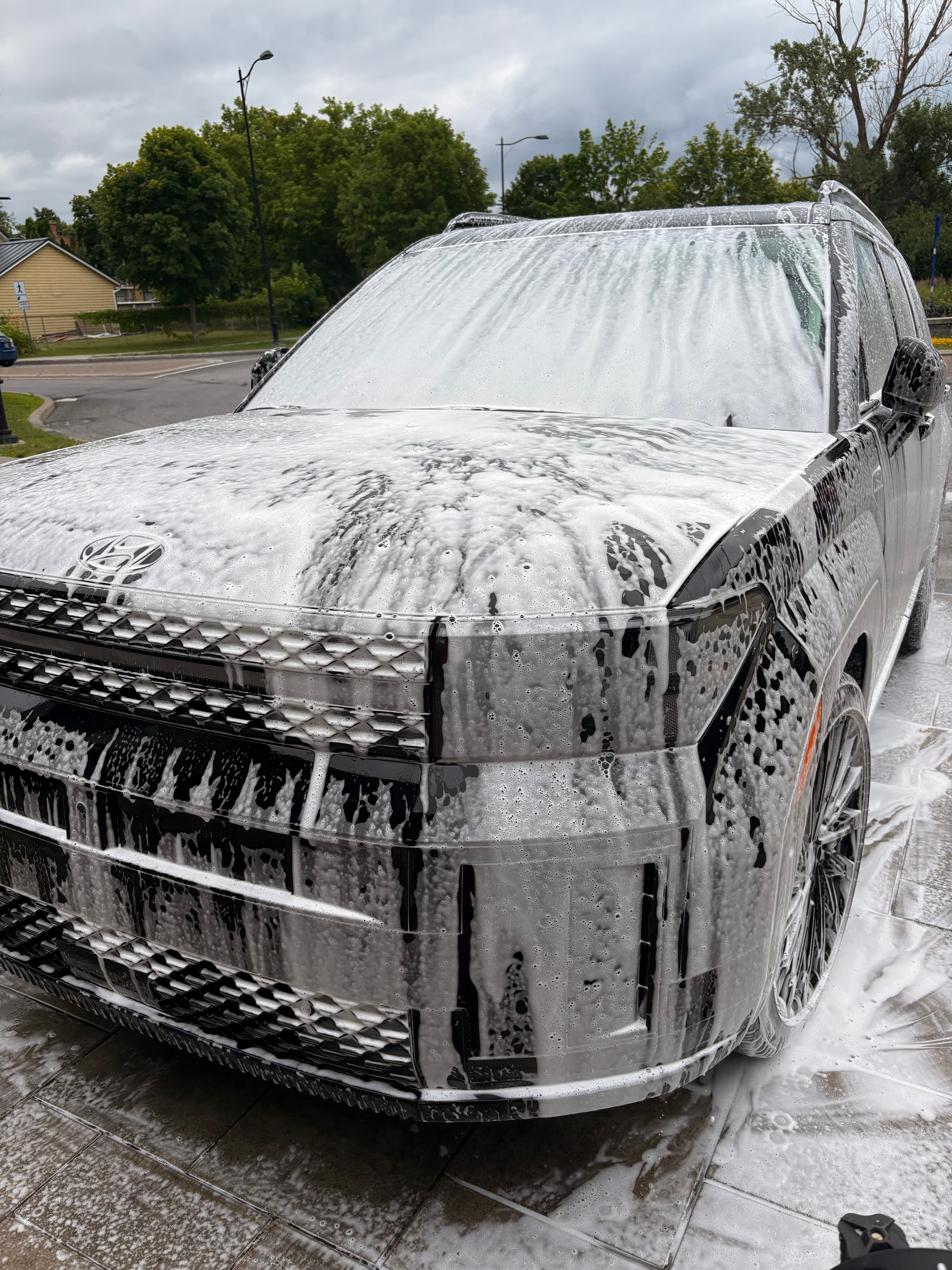 Thick white soap foam covers the front grille and windshield of a black Hyundai SUV.