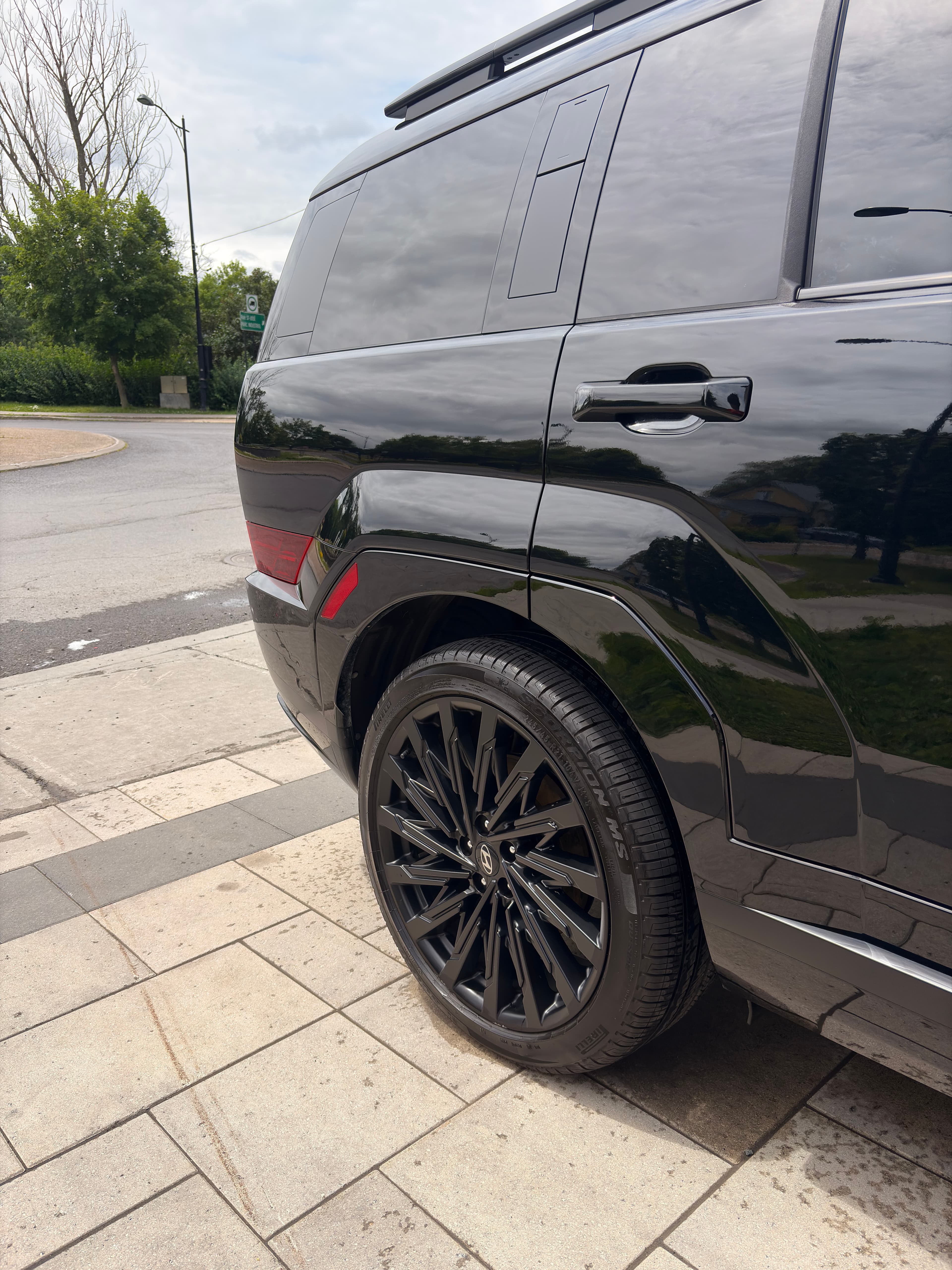 Glossy black SUV with stylish multi-spoke wheels parked on a light-colored stone sidewalk.